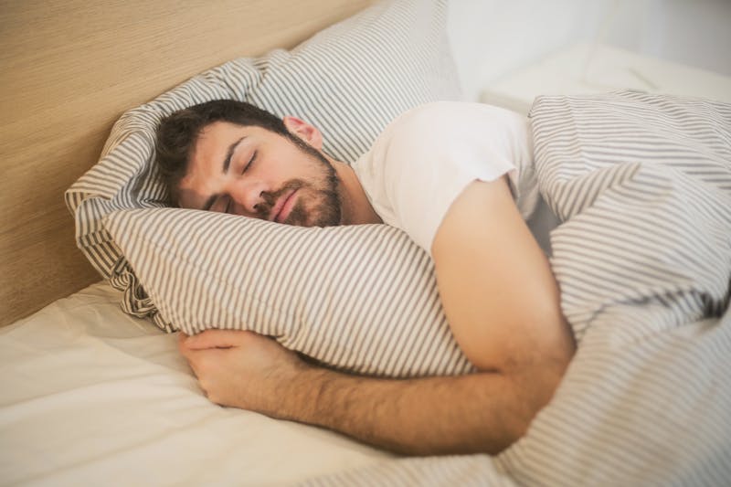 Young man sleeping peacefully in a bed with grey and white striped bedding